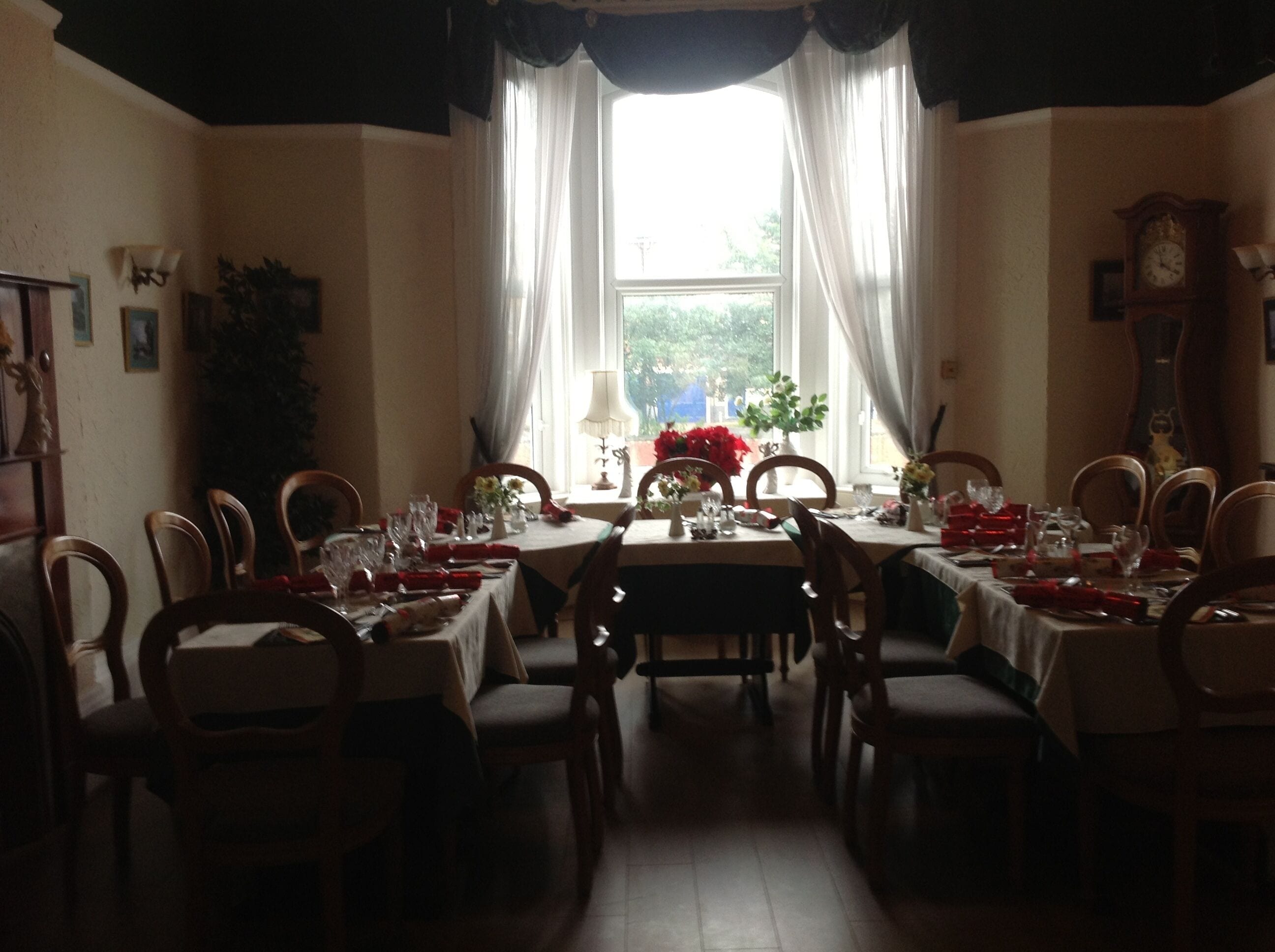 A dining room with a large window, multiple tables set for dining, and a clock on the wall.