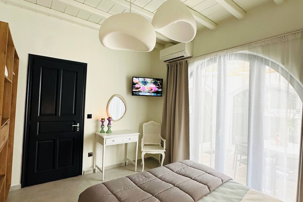 A bedroom with a large bed, a desk, a chair, a TV, and a window with curtains.