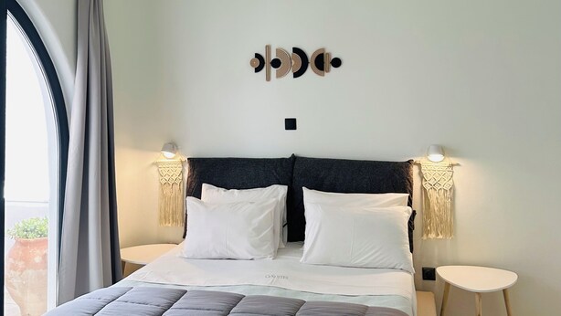 Un dormitorio moderno con una cama grande, dos mesitas de noche, una lámpara de techo y un adorno en la pared.