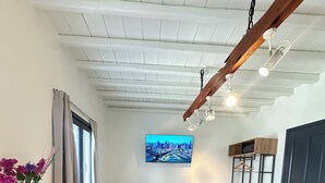 Una sala moderna con un sofá, una mesa de centro, una mesita auxiliar, un televisor montado en la pared y un estante de madera.