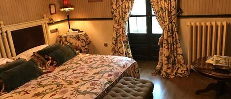 Un dormitorio con cama, mesita de noche, lámpara, banco y radiador.