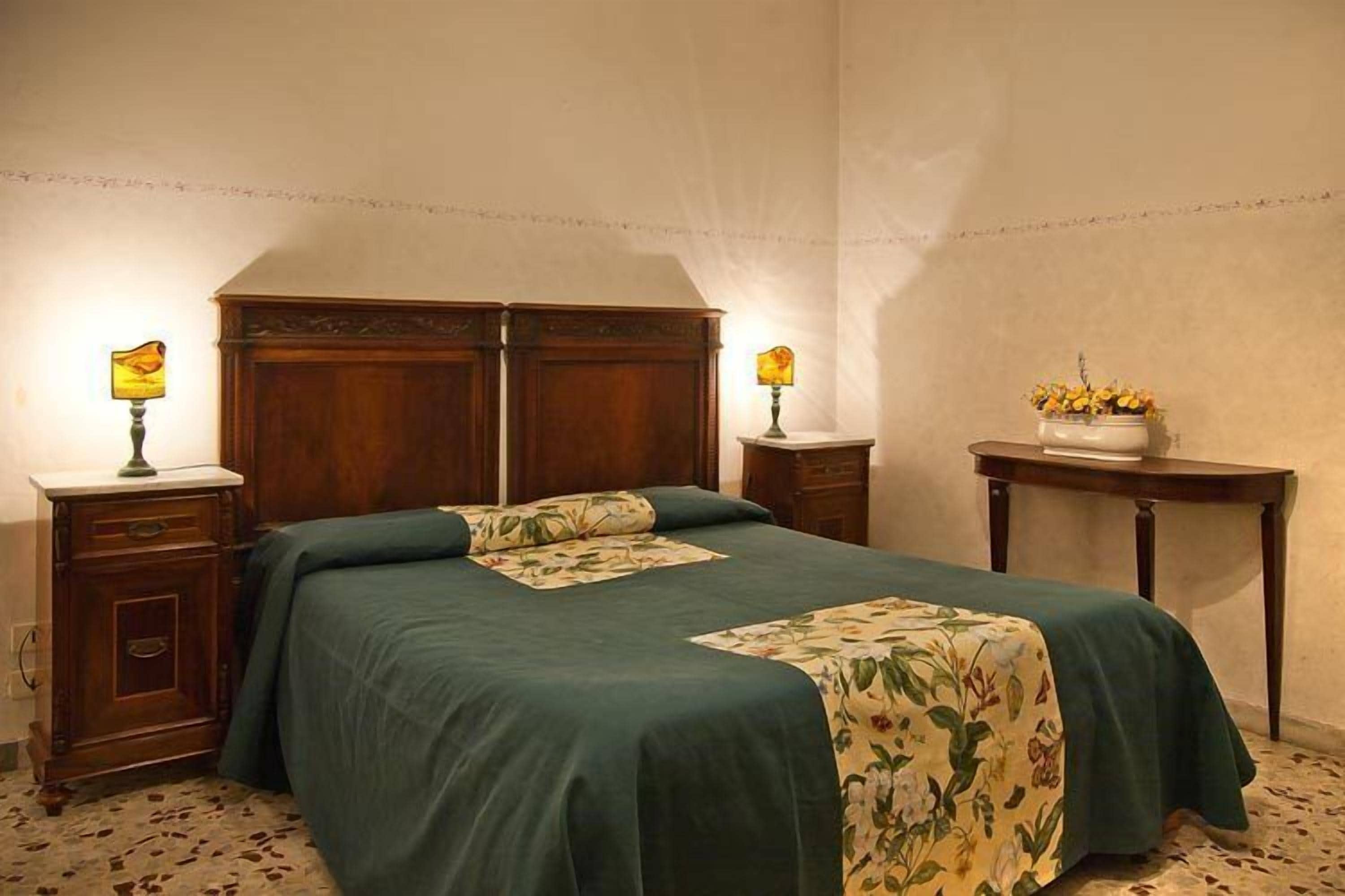 A bedroom with a large bed, two bedside tables, a nightstand, and a small table with a vase of flowers.