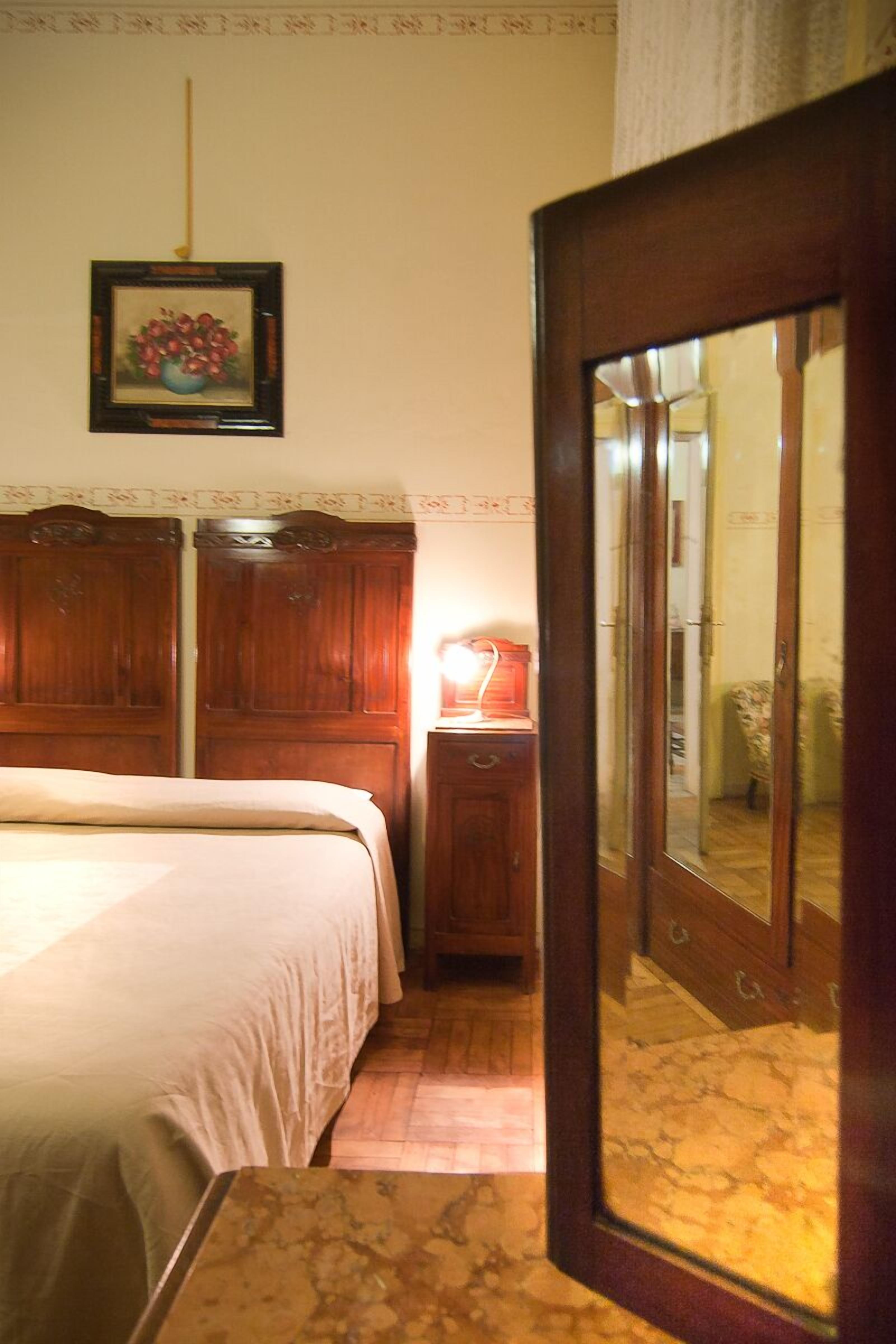 A bedroom with a bed, a nightstand, a mirror, and a framed picture on the wall.