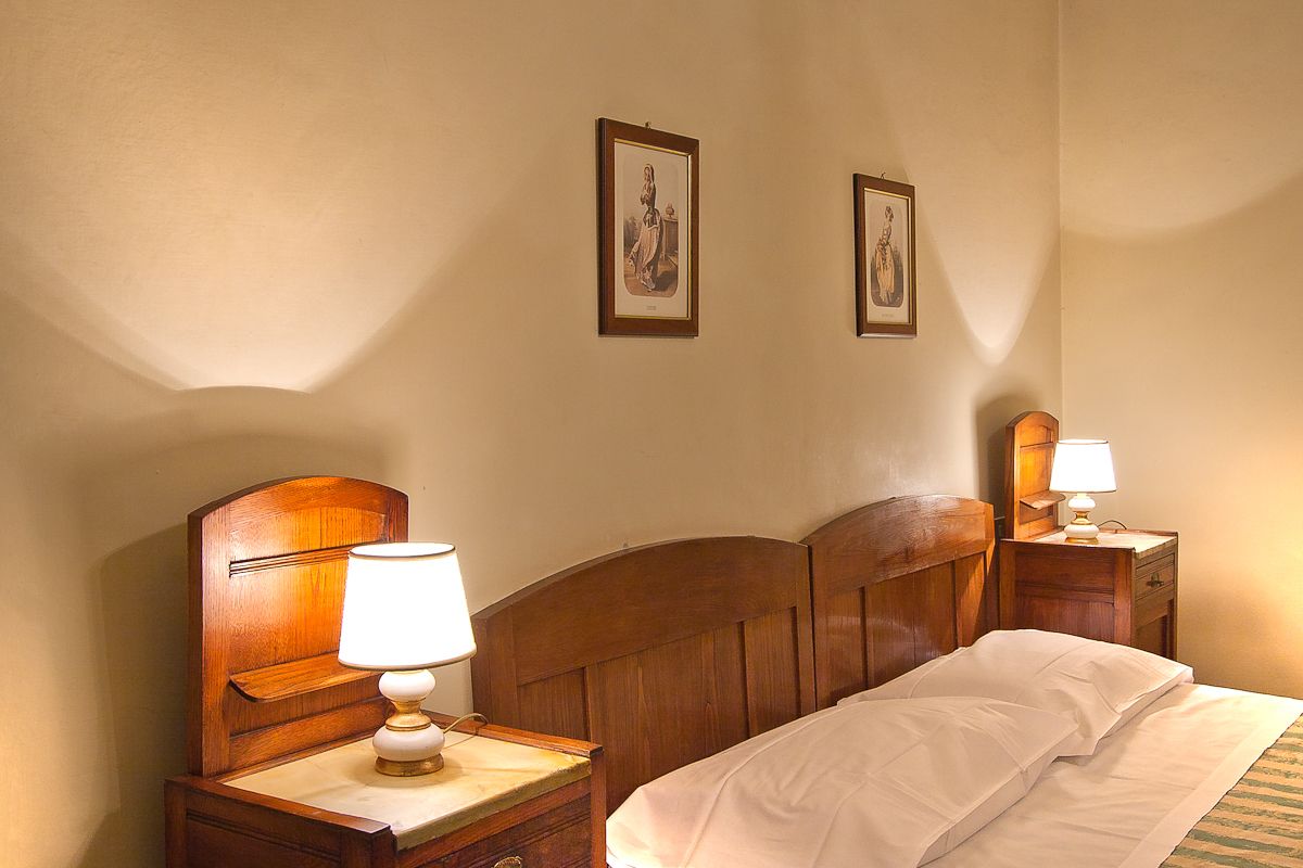 Een hotelkamer met een houten hoofdeinde, twee nachtkastjes met lampen en twee ingelijste foto’s aan de muur.