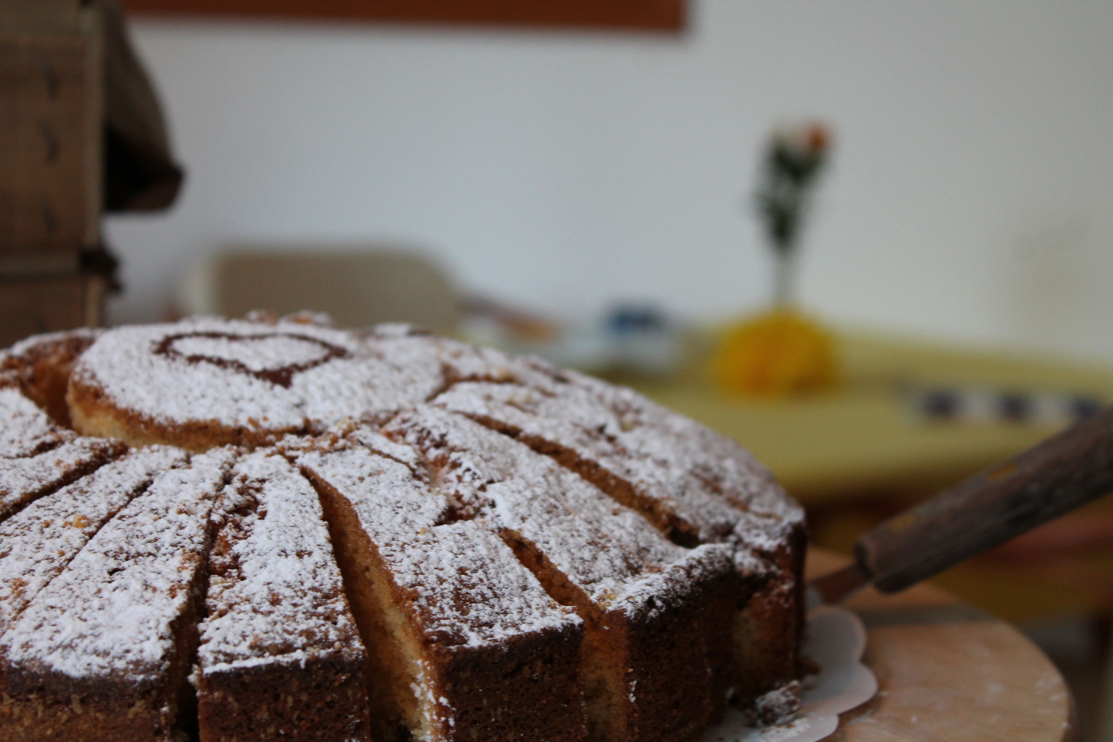 A round cake with powdered sugar on top, placed on a wooden board.