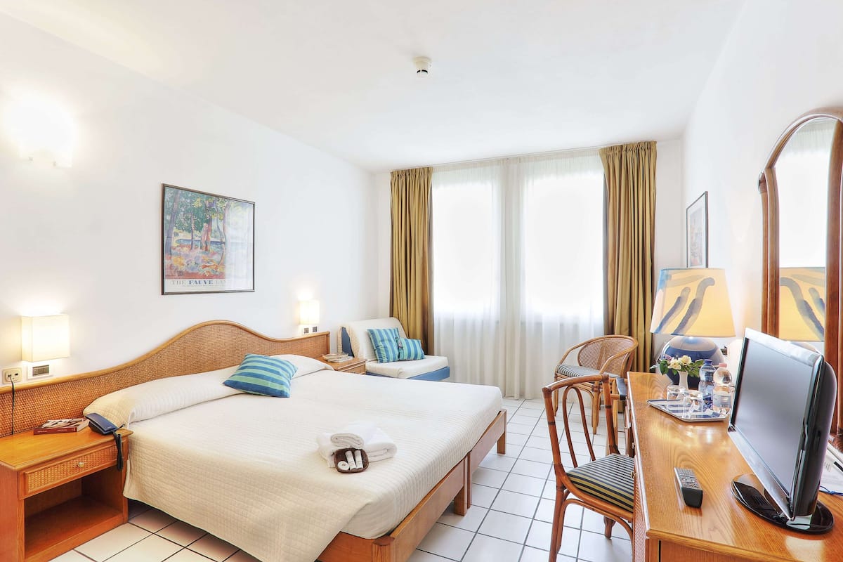 Una habitación de hotel con una cama grande, un escritorio con televisión, una silla y una ventana con cortinas.