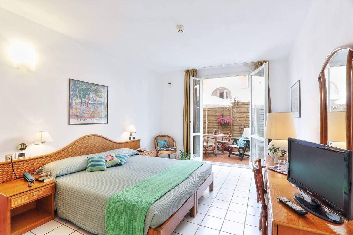 Habitación de hotel con cama, mesita de noche, lámpara, televisión y vistas al exterior.