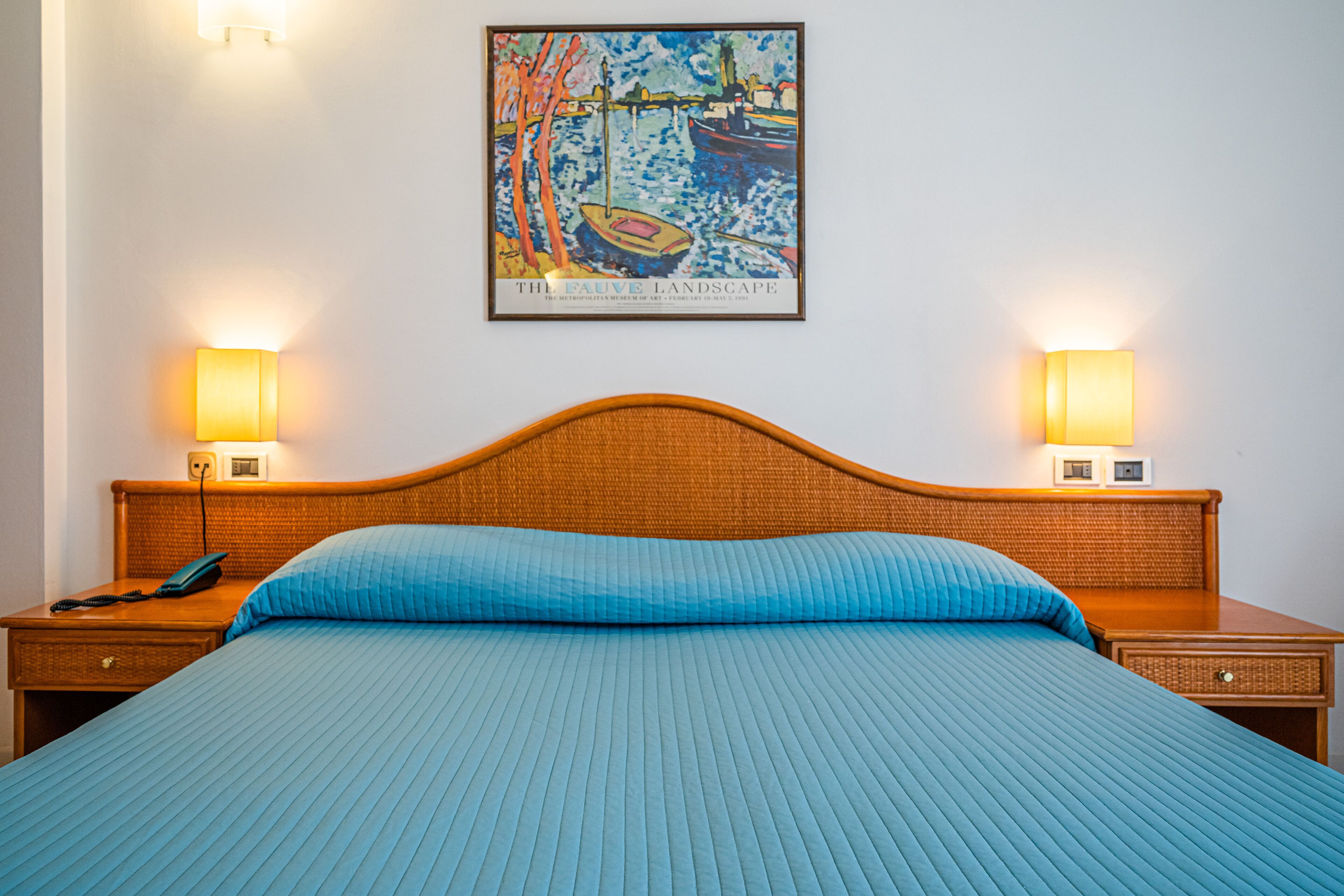 Une chambre d’hôtel avec un grand lit, deux tables de chevet, une tête de lit et une œuvre d’art encadrée au mur.
