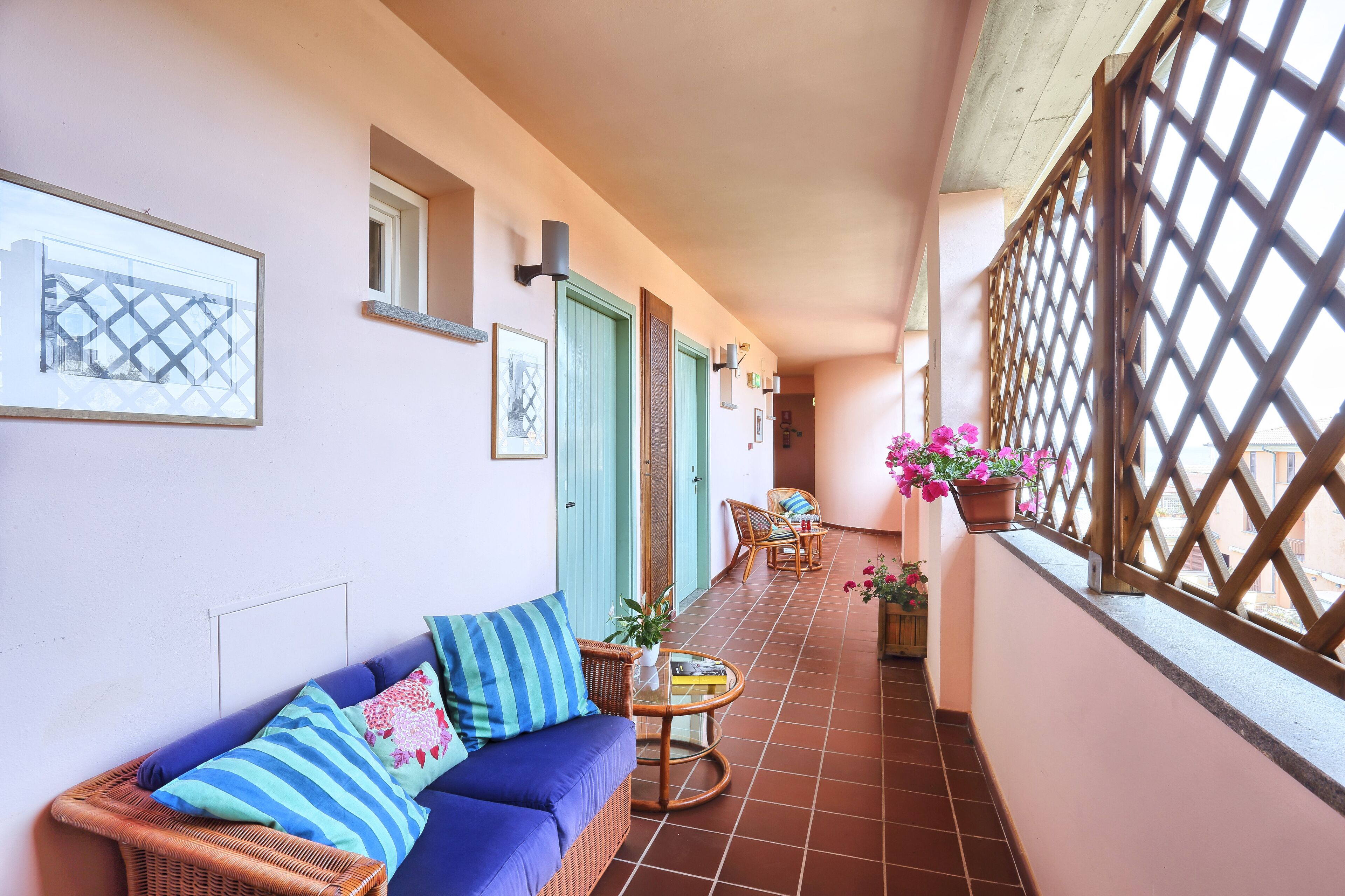 A narrow balcony with a wicker sofa, a small round table, and potted plants.