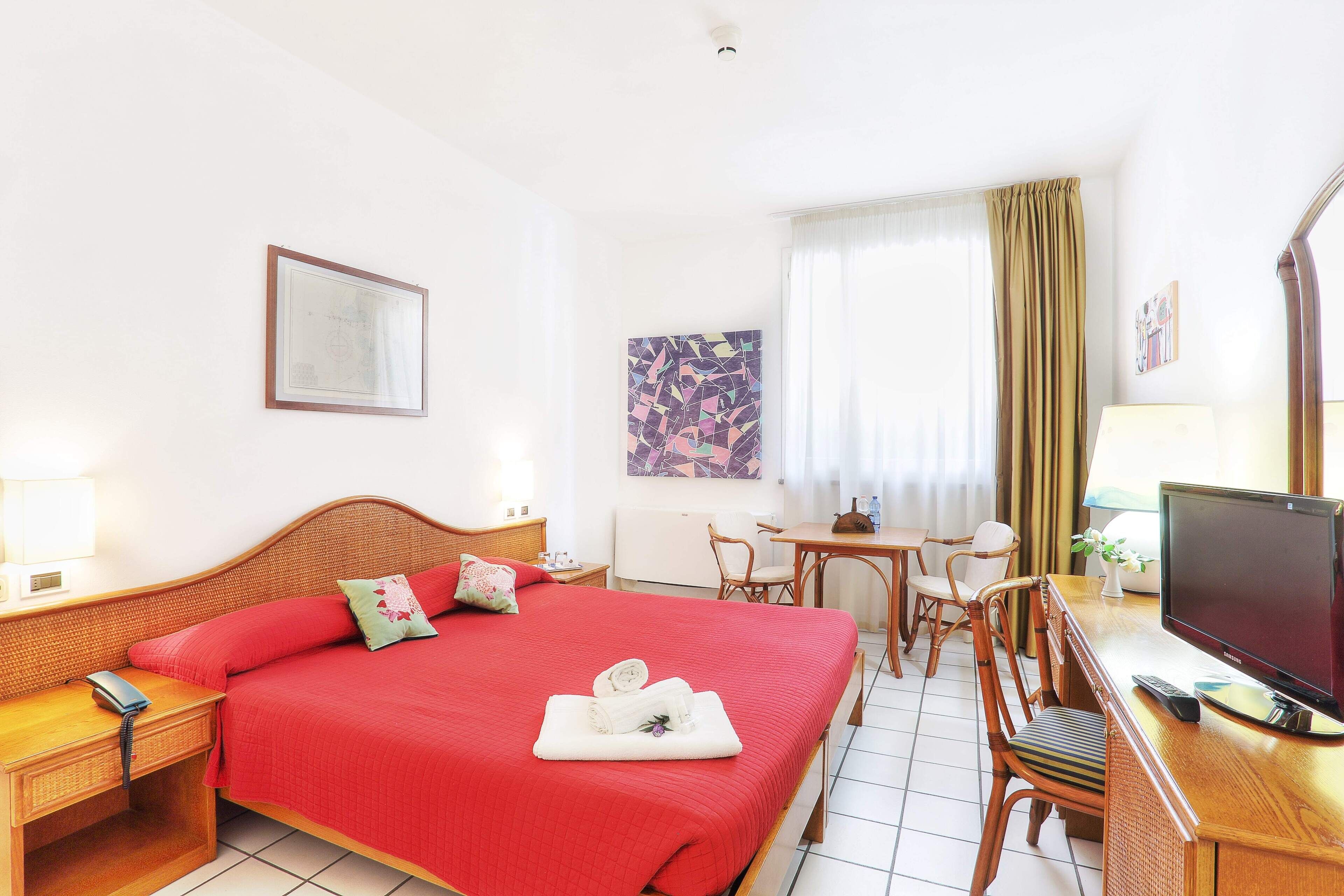 A hotel room with a large bed, a desk with a computer, a chair, and a television.