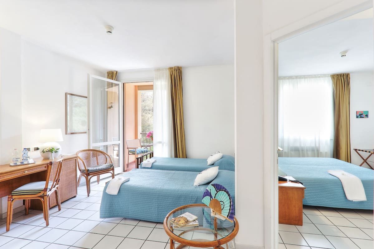 Habitación de hotel con dos camas, un escritorio con silla, una mesita y una ventana con cortinas.