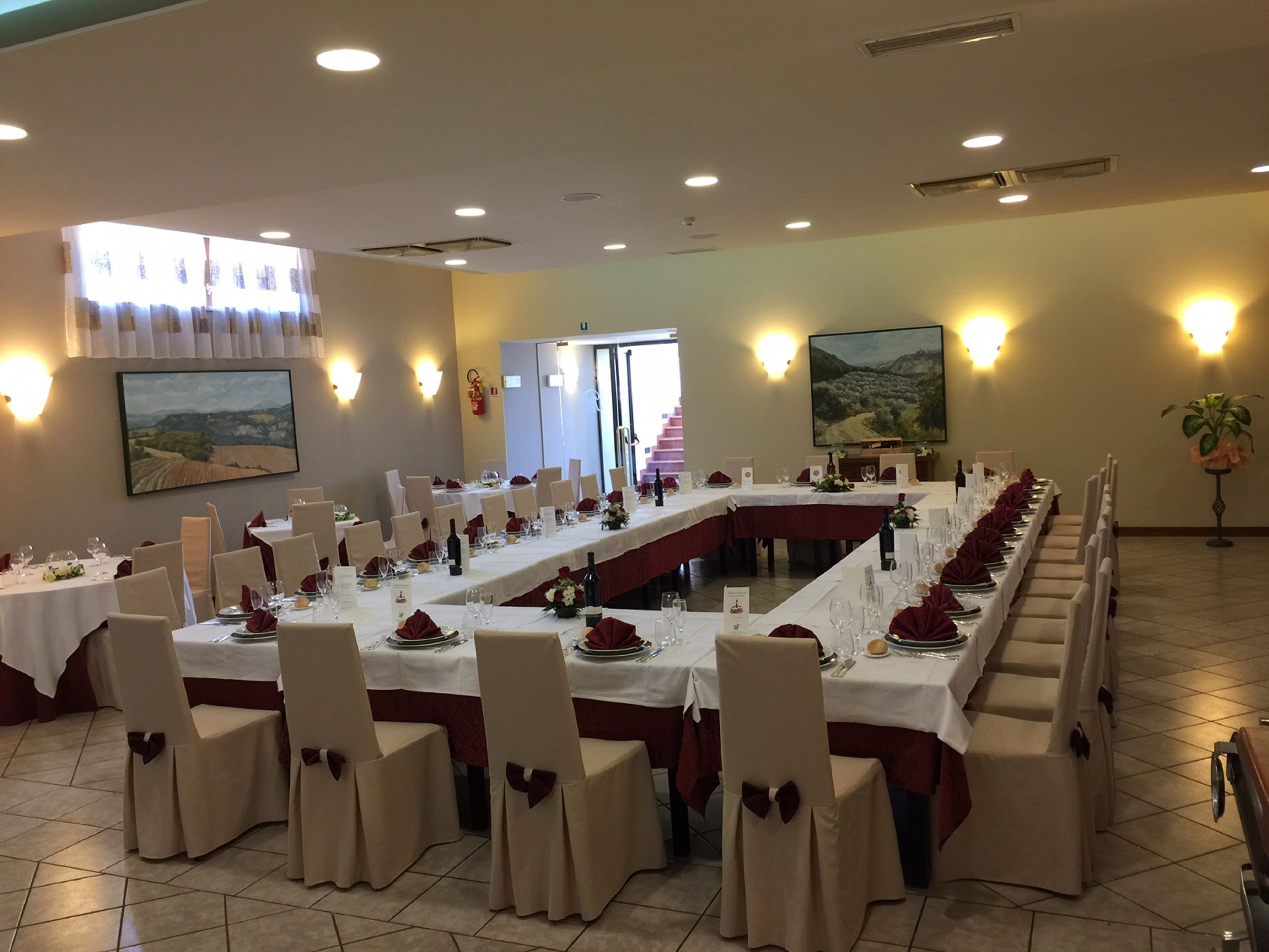 A long dining table with white tablecloths and red napkins, surrounded by chairs with beige covers and bows.