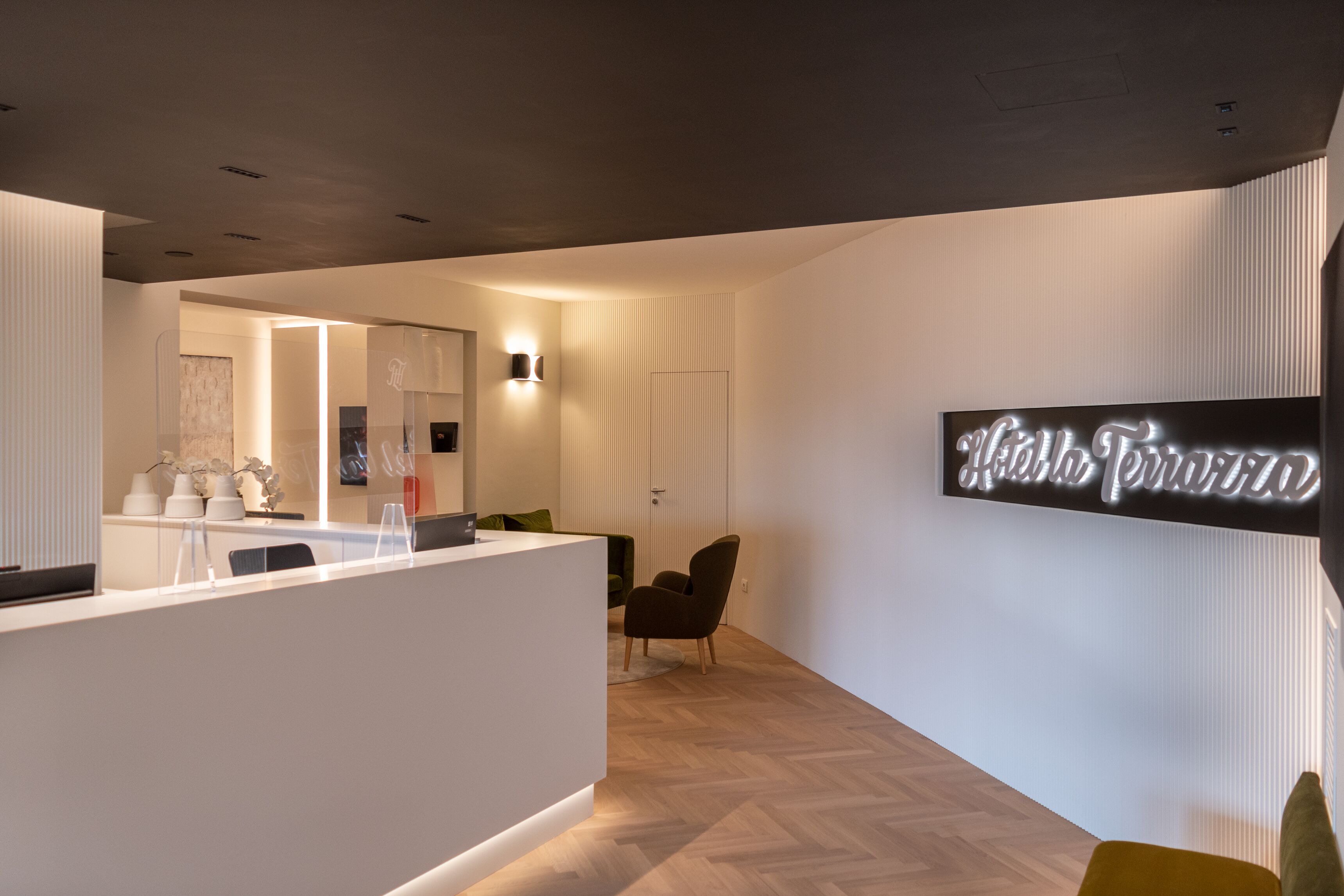 A modern reception area with a white reception desk, a green chair, and a wall-mounted sign that reads "Hotel Terra."