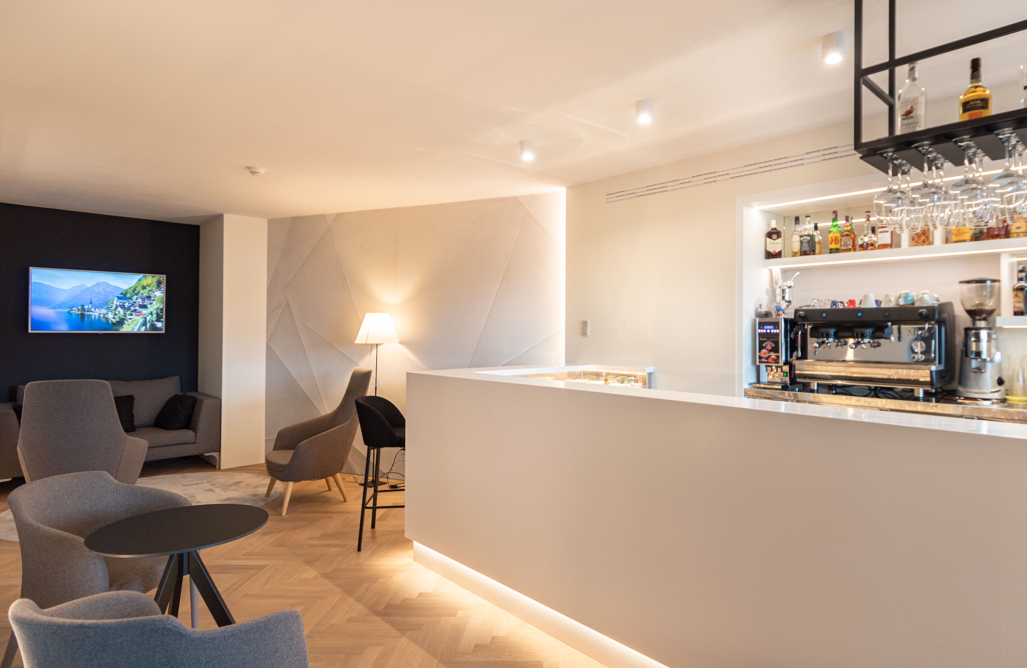 A modern bar area with a flat-screen TV, bar stools, and a coffee machine.