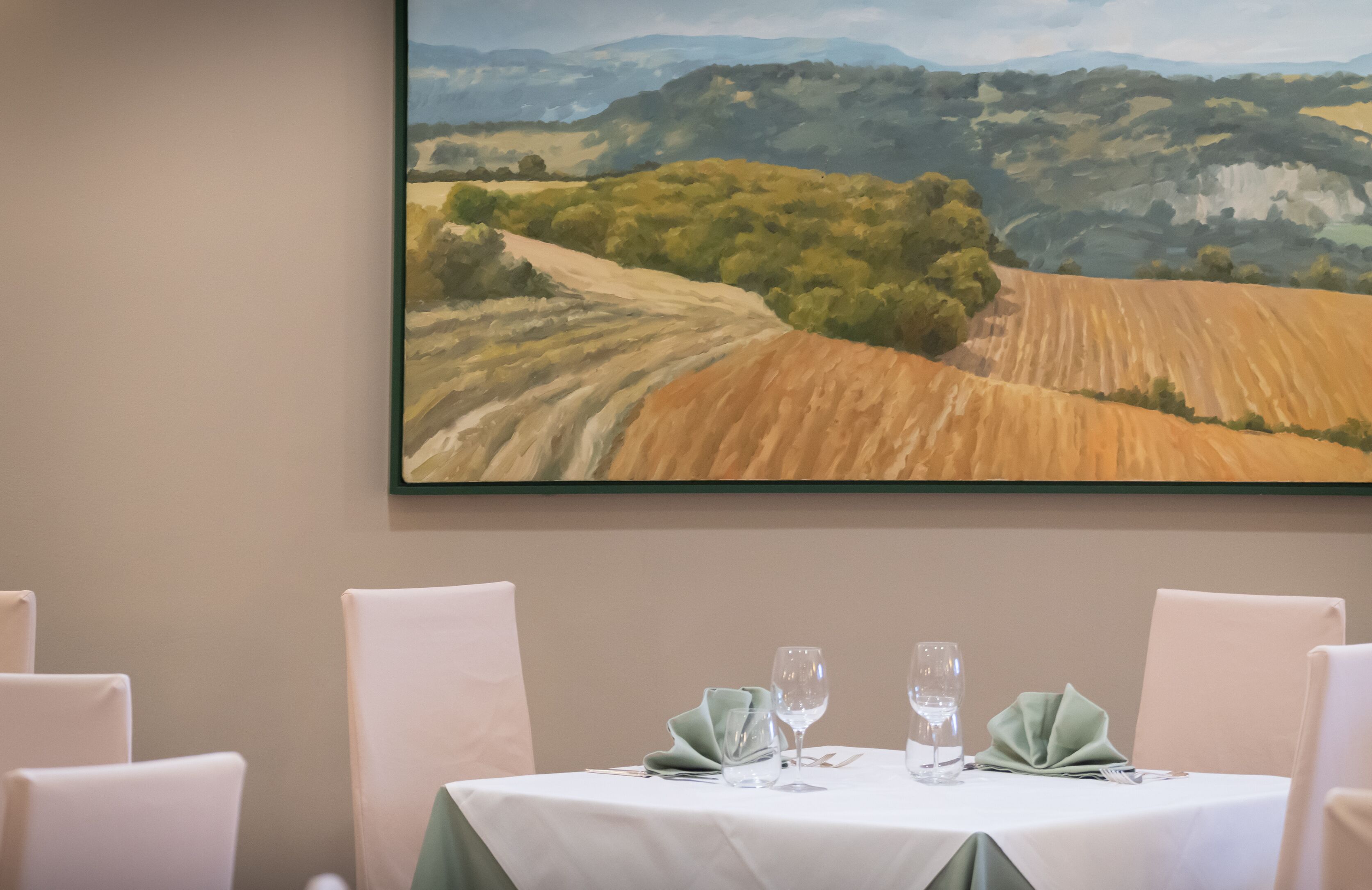 Une table à manger dressée avec une nappe blanche, deux serviettes vertes et deux verres à vin.