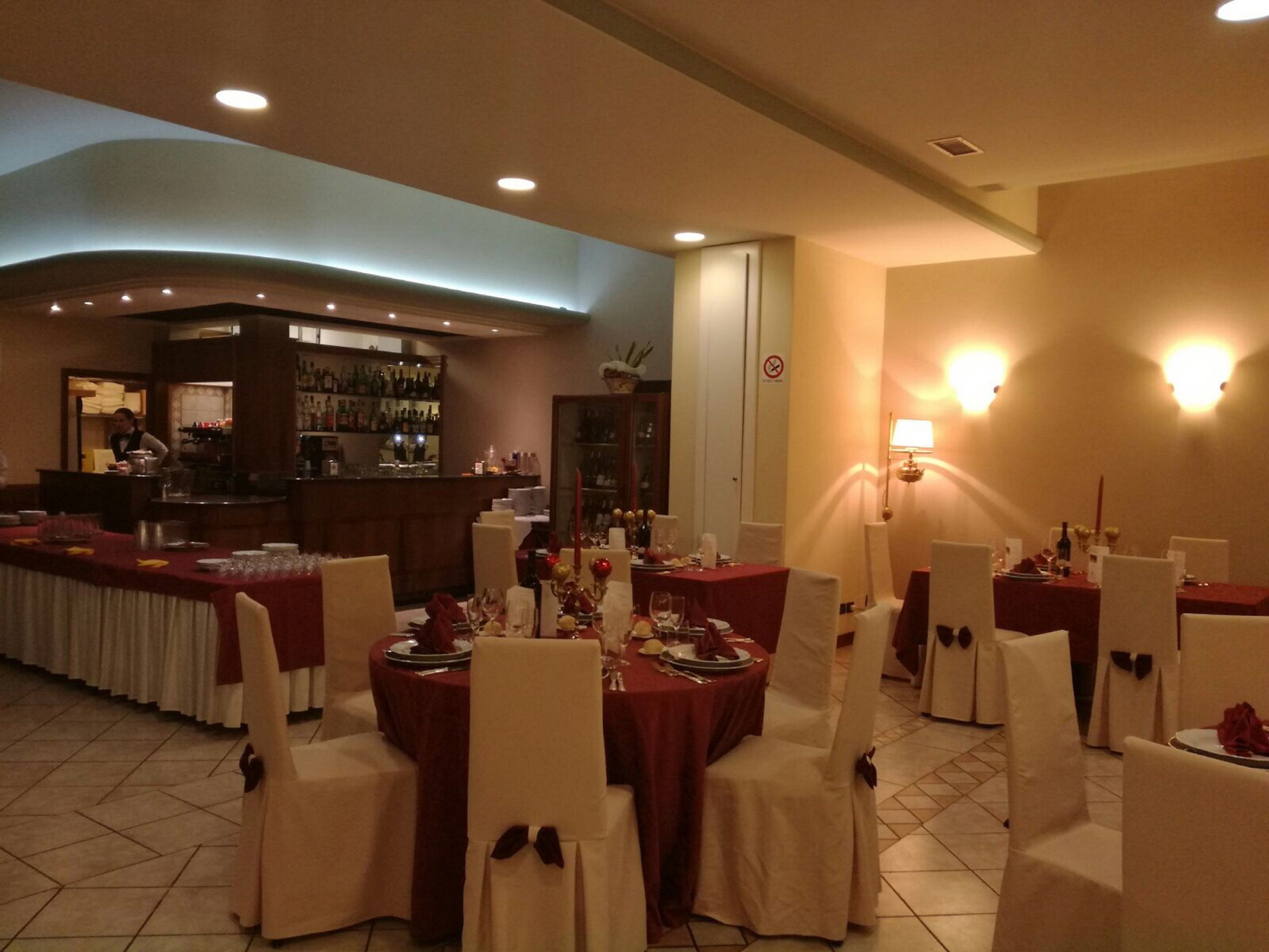 Een restaurant met ronde tafels, witte stoelen en een bar op de achtergrond.