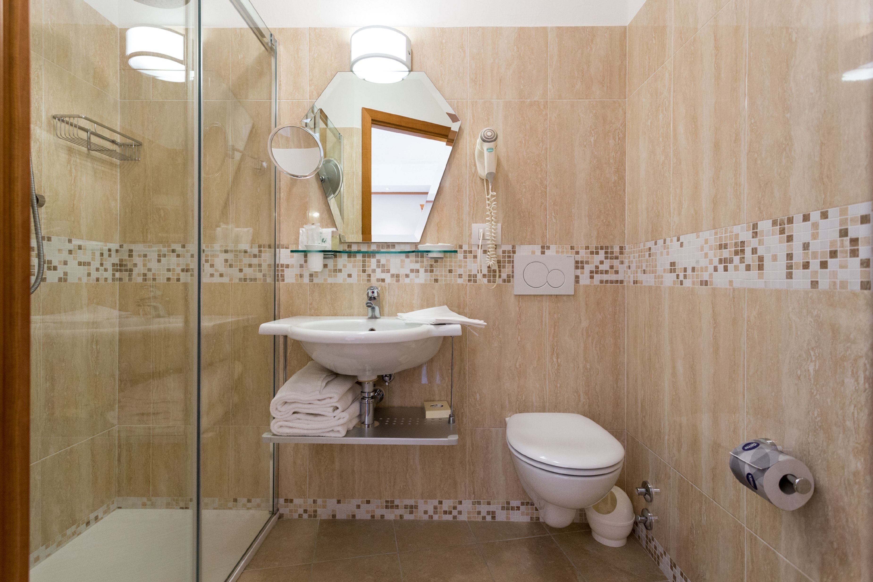 A bathroom with a glass shower enclosure, a sink with a mirror, a toilet, and a toilet paper holder.