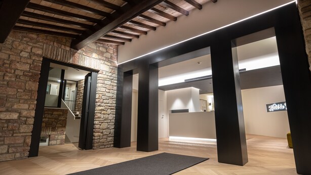 Un interior espacioso con vigas de madera a la vista, paredes de piedra y columnas negras modernas.