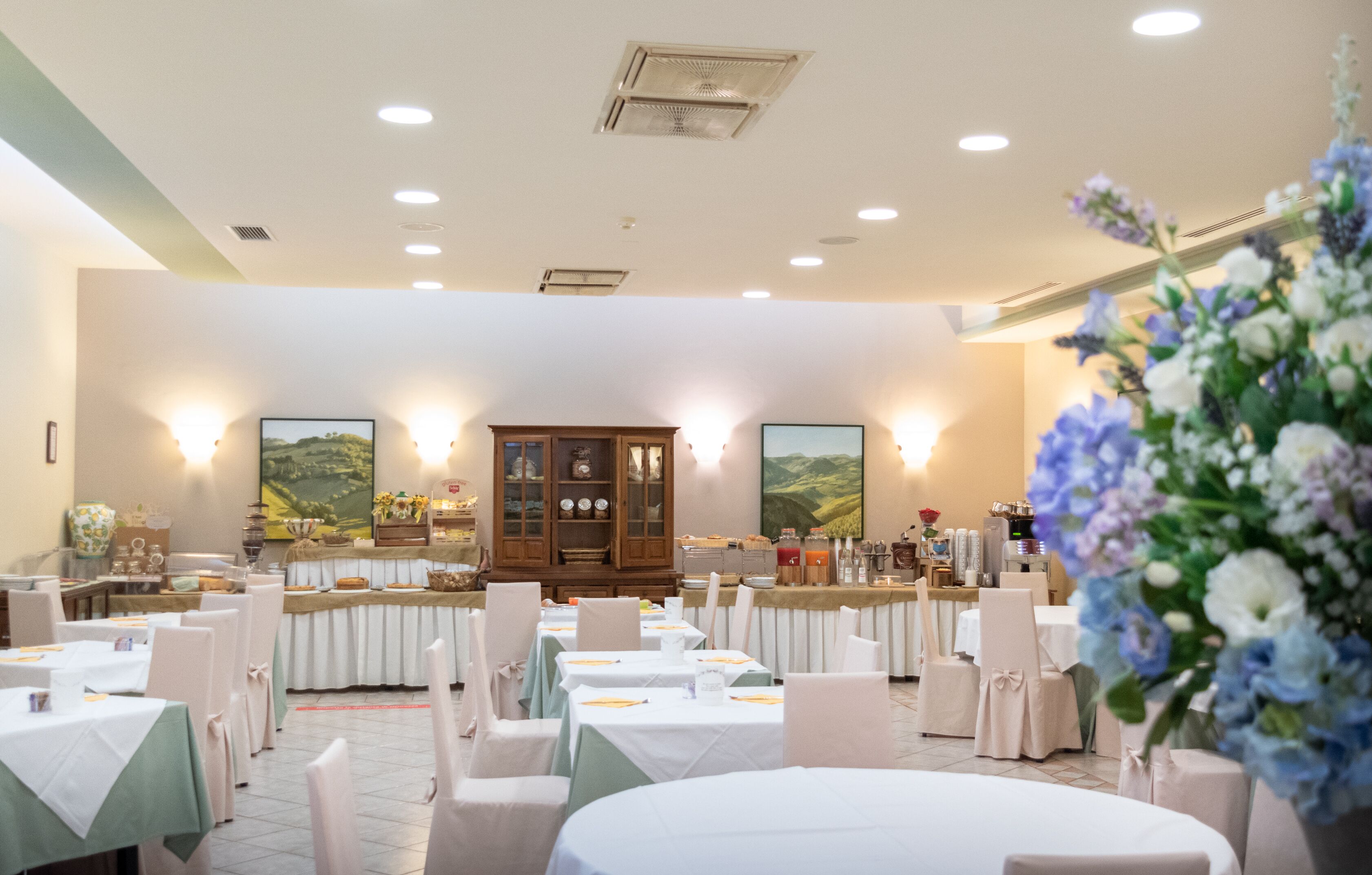 Une salle de banquet avec des tables rondes, des chaises blanches et un espace buffet.
