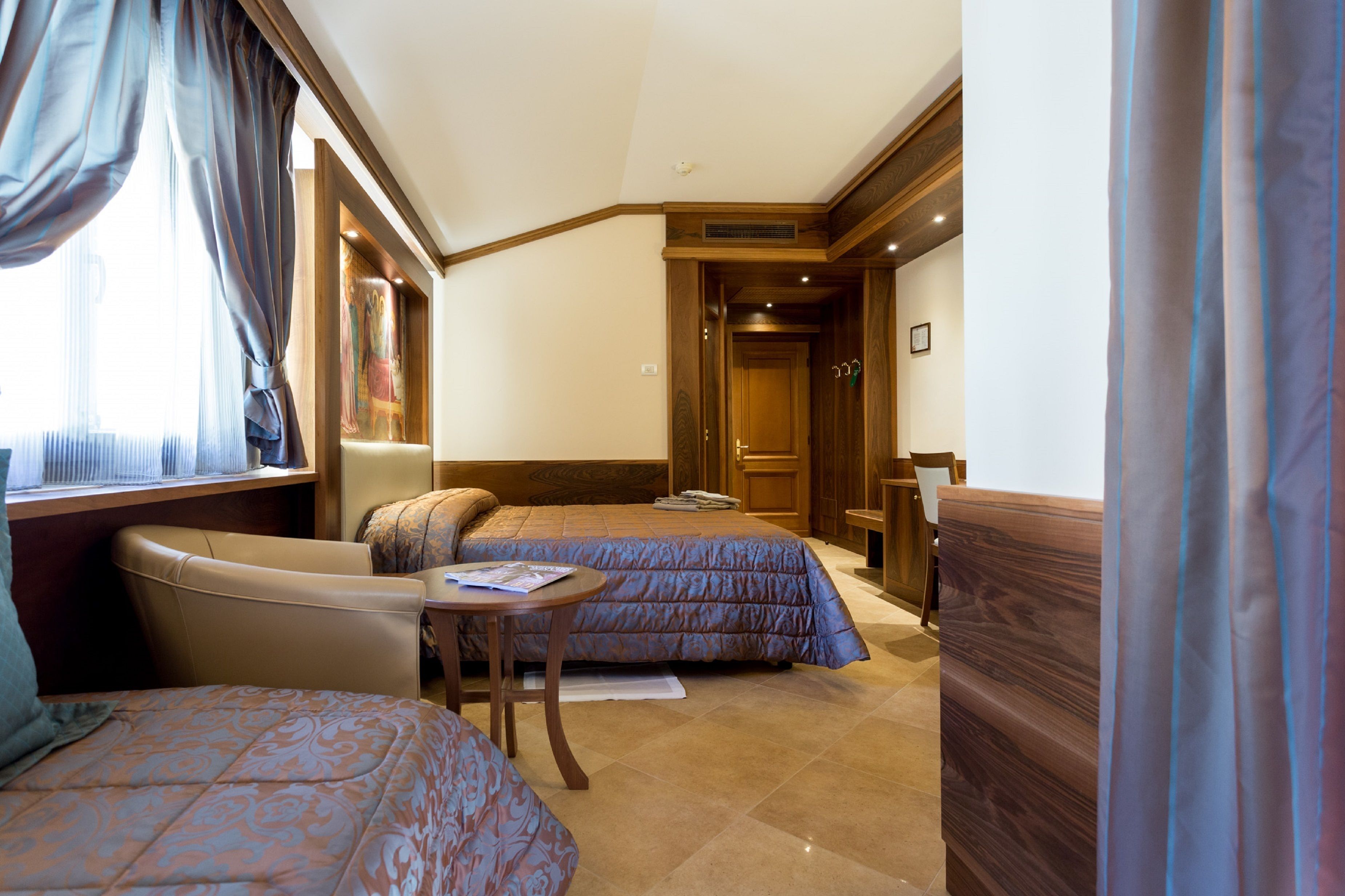 A hotel room with two beds, a sofa, a small table, and a wooden wardrobe.