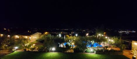A nighttime view of a residential area with illuminated buildings and a swimming pool.