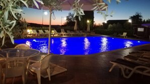 Piscina exterior con sillas de descanso y una mesa, rodeada de olivos y una puesta de sol al fondo.