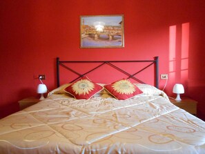 A bed with a patterned bedspread, two pillows with sunflowers, a framed picture on the wall, and two bedside lamps. - Hotel Aline (Florence)
