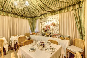 Comedor con mesas dispuestas para el desayuno, sillas de mimbre y un bufé con diversas opciones de comida.