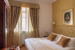 Una habitación de hotel con una cama, cortinas, un cuadro en la pared y una mesita con una taza.
