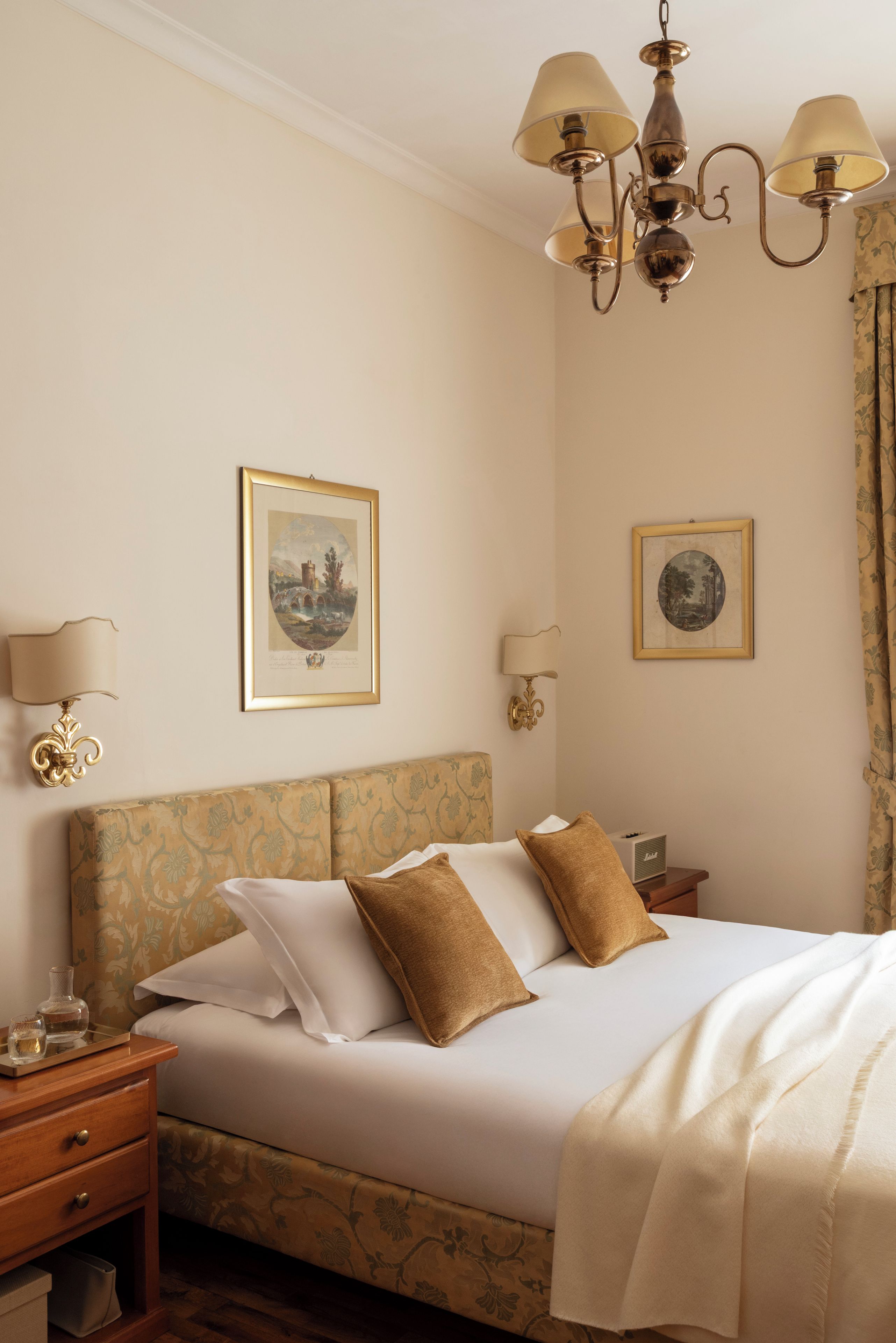 Una habitación de hotel con una cama, una mesita de noche, una lámpara y dos cuadros colgados en la pared.
