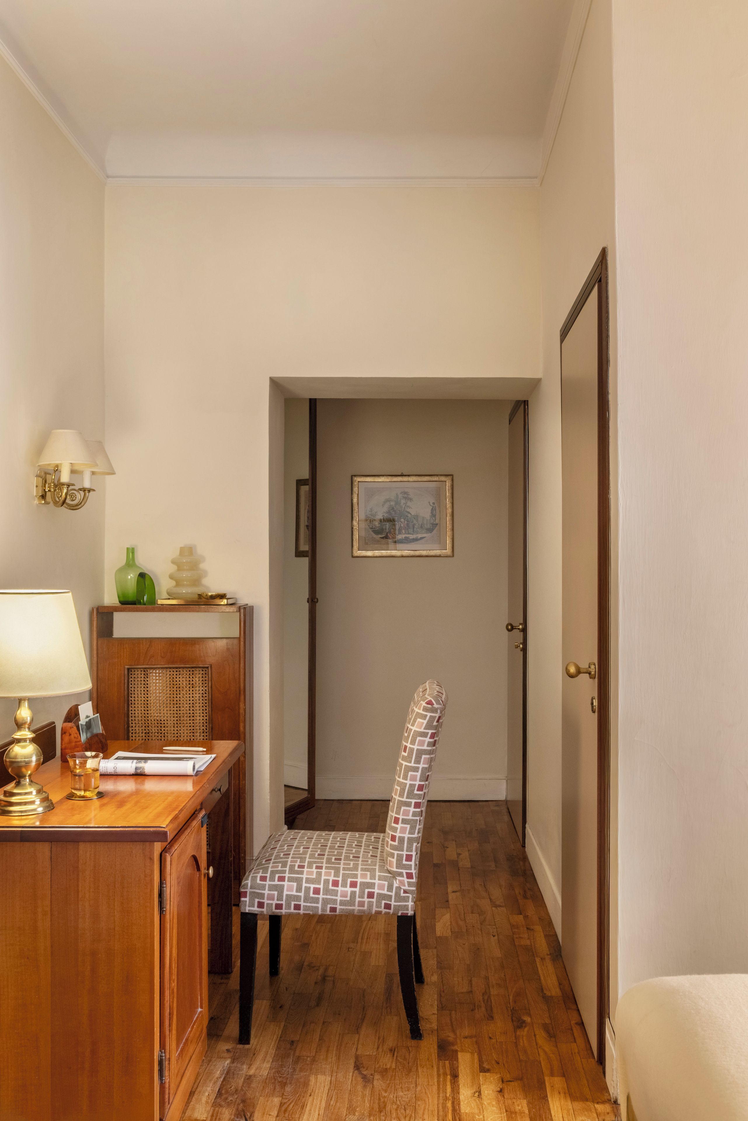 Un pasillo con un escritorio de madera, una silla, una lámpara y una puerta.