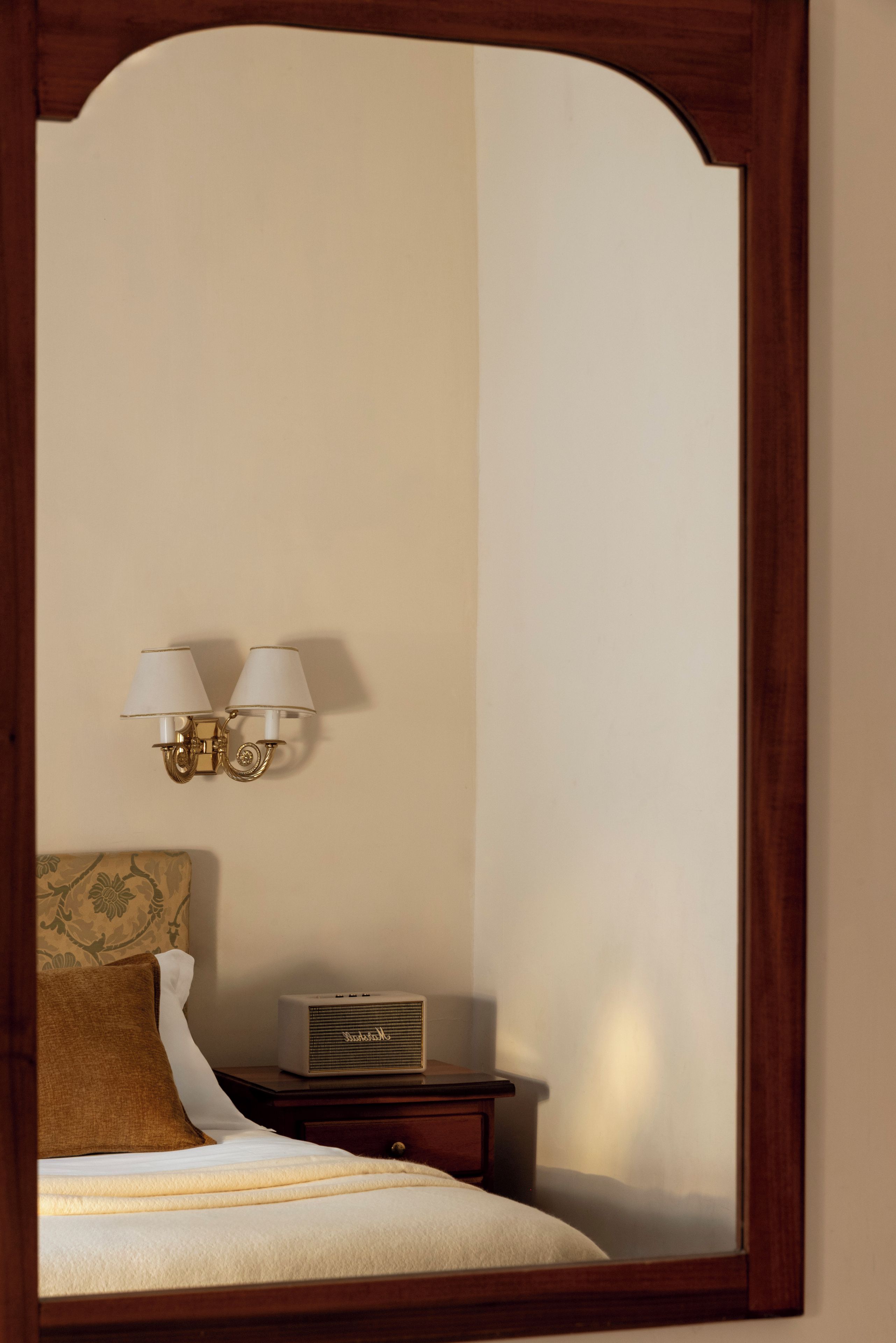 A bedroom with a bed, a nightstand, a lamp, and a mirror.