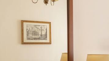Quarto de hotel com cama, mesa de cabeceira, abajur, quadro pendurado na parede e espelho.