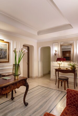 A room with a wooden desk, a chair, a vase with flowers, a framed picture on the wall, and a mirror with a red lamp. - Hotel Cortina (Rome)