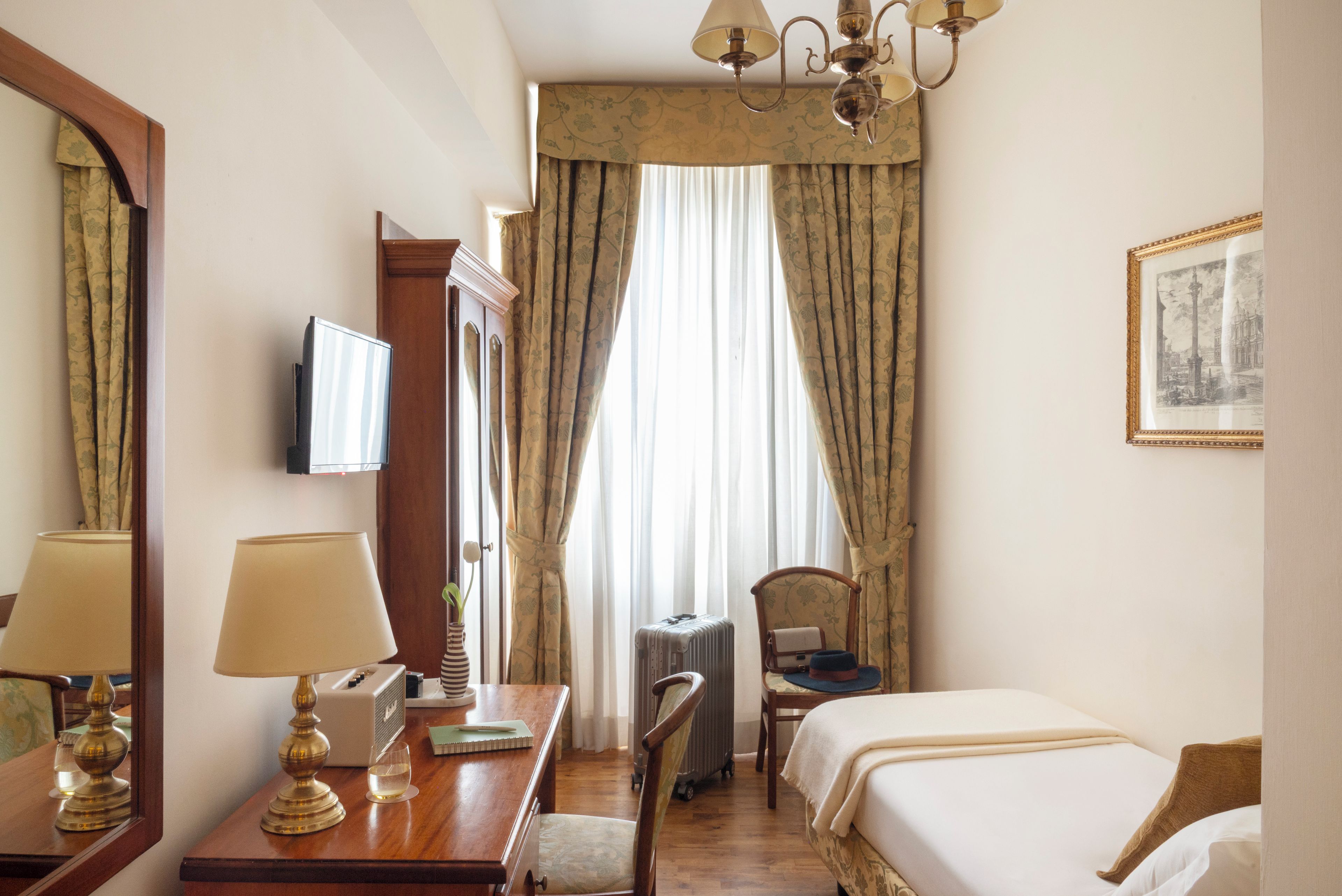 Een hotelkamer met een bed, bureau, stoel, lamp en een televisie.