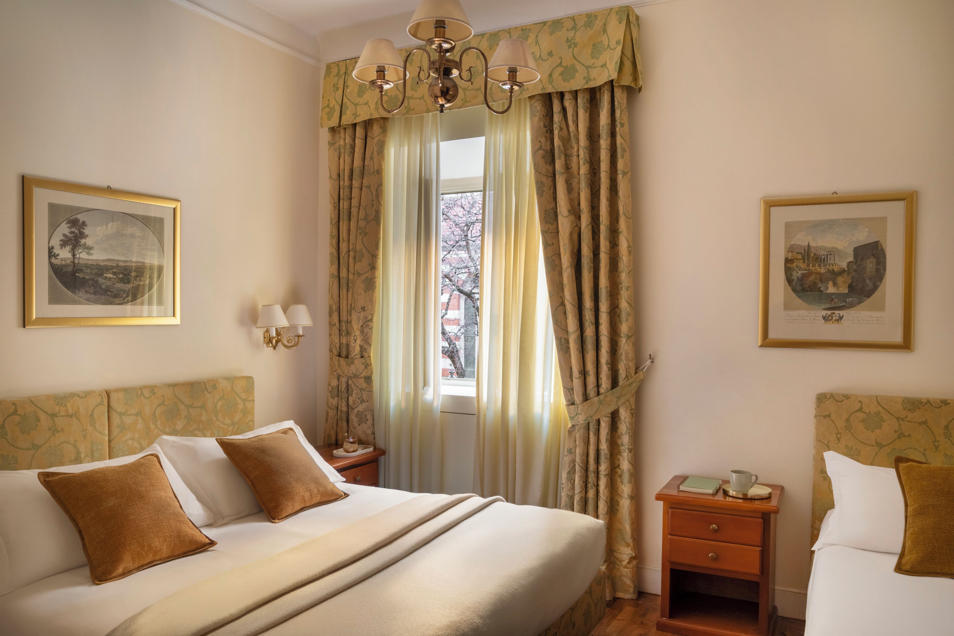 Une chambre d’hôtel avec un grand lit, deux tables de chevet, une petite table et une fenêtre avec des rideaux.