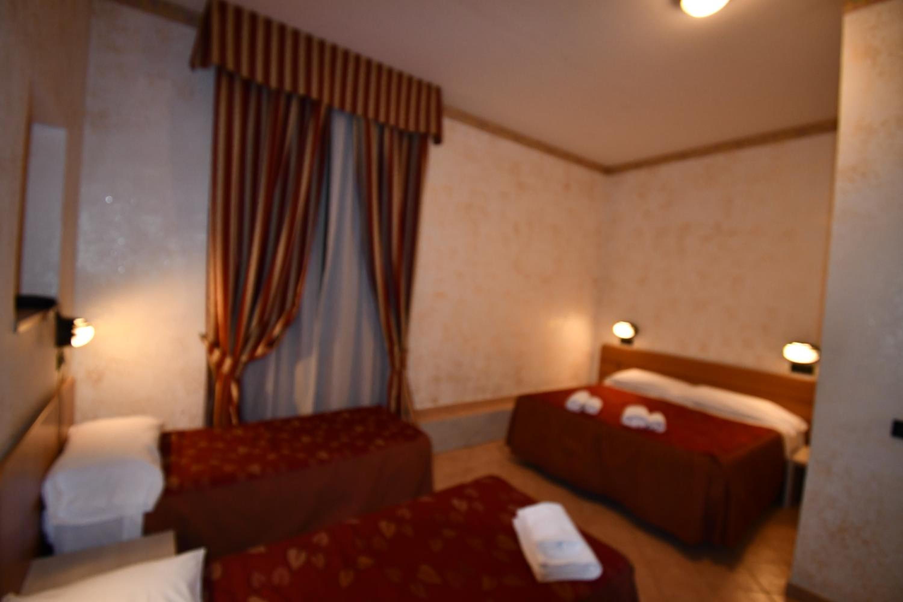 A hotel room with two beds, a window with curtains, and bedside lamps.