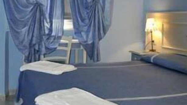 Una camera da letto con un letto, un comodino, una lampada e tende.
