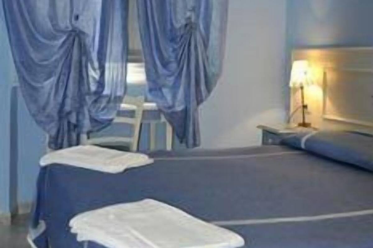 Un dormitorio con cama, mesita de noche, lámpara y cortinas.