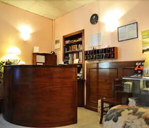 Un área de recepción con un escritorio de madera, una estantería, un reloj y un certificado enmarcado en la pared.