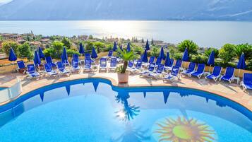 Un área de piscina con sillas reclinables azules y sombrillas, con vistas panorámicas a un lago y montañas.