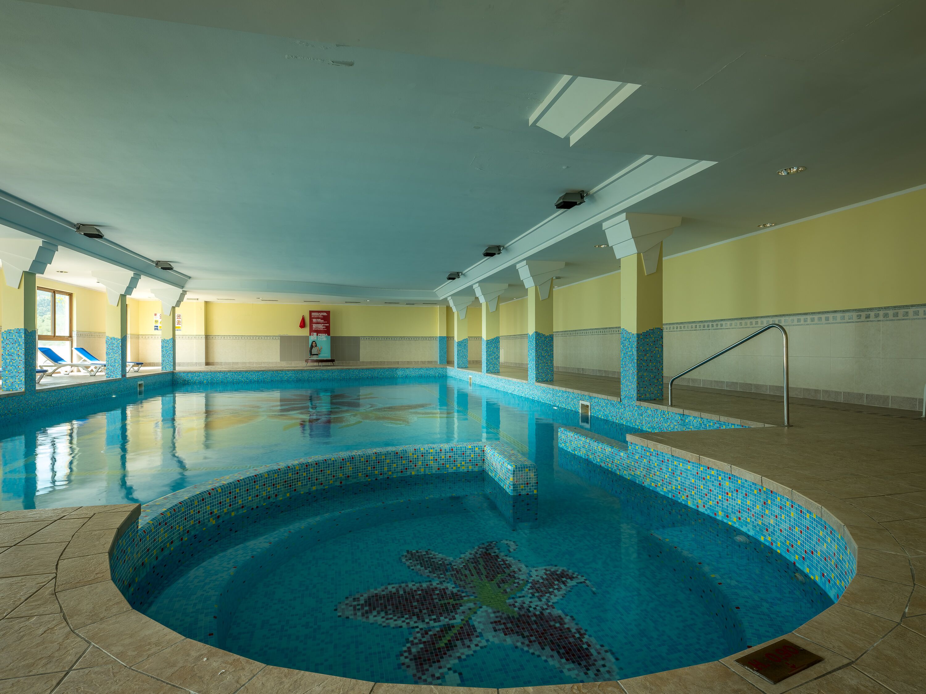 Une grande piscine intérieure à l’eau d’un bleu limpide, avec des murs carrelés et un toit ouvrant.