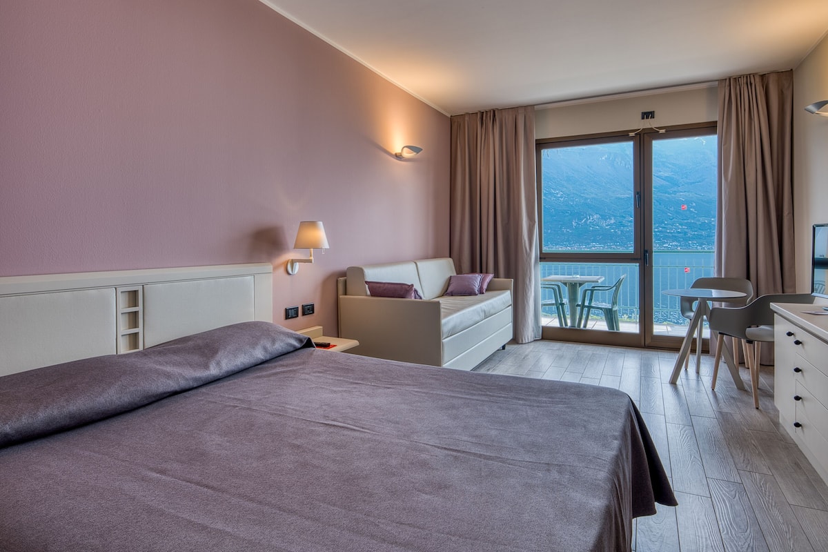 A hotel room with a bed, a desk, a chair, a table, and a view of the outdoors.