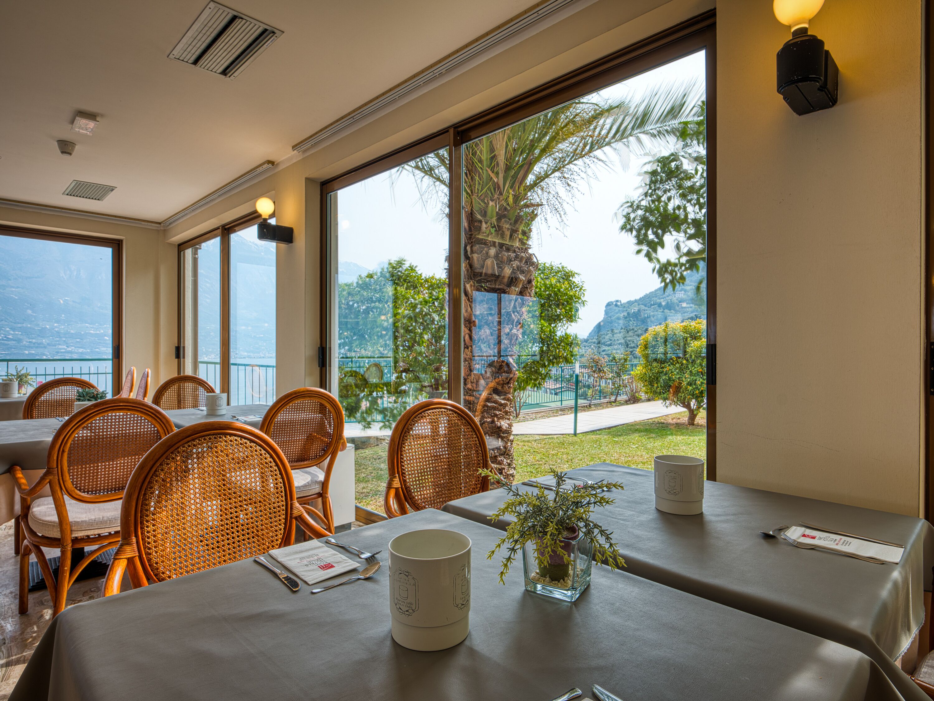 Comedor con sillas de mimbre y una mesa lista para dos, con vistas panorámicas a una montaña y palmeras.
