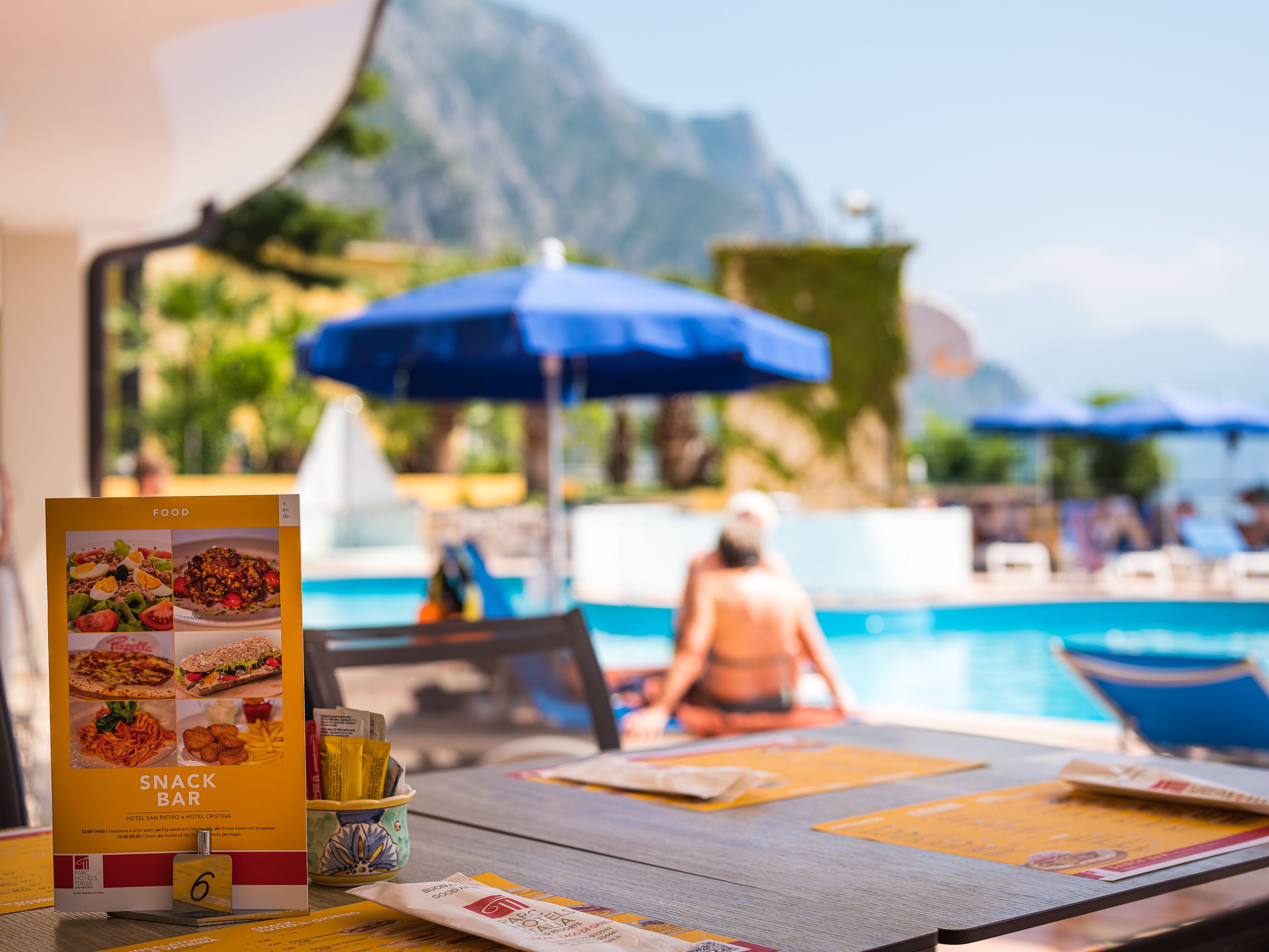 A poolside table with a snack bar menu, a glass of water, and a menu on a wooden table.