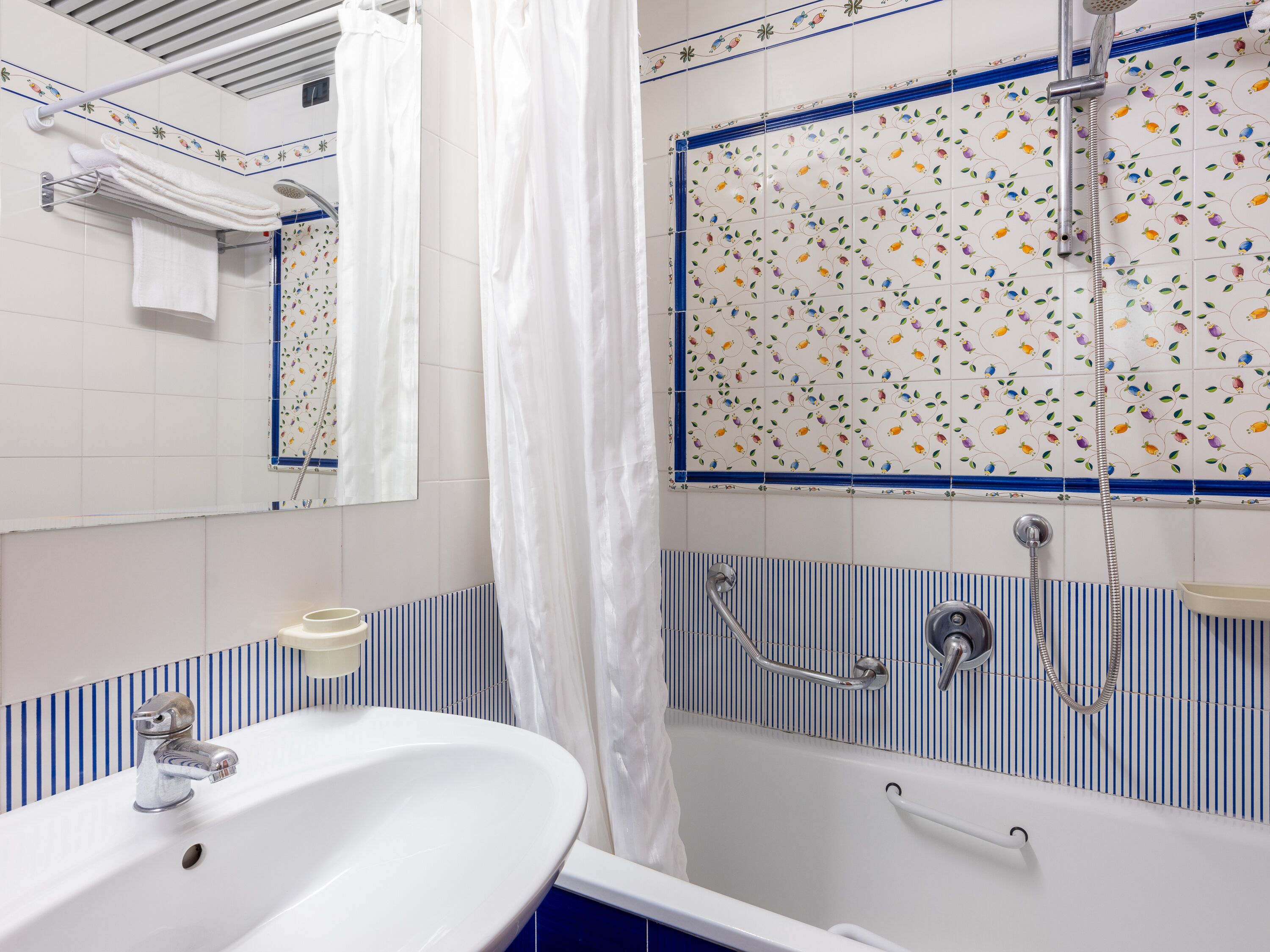 Une salle de bain avec un lavabo blanc, une douche ornée de motifs floraux en carreaux et un mur à rayures bleues et blanches.