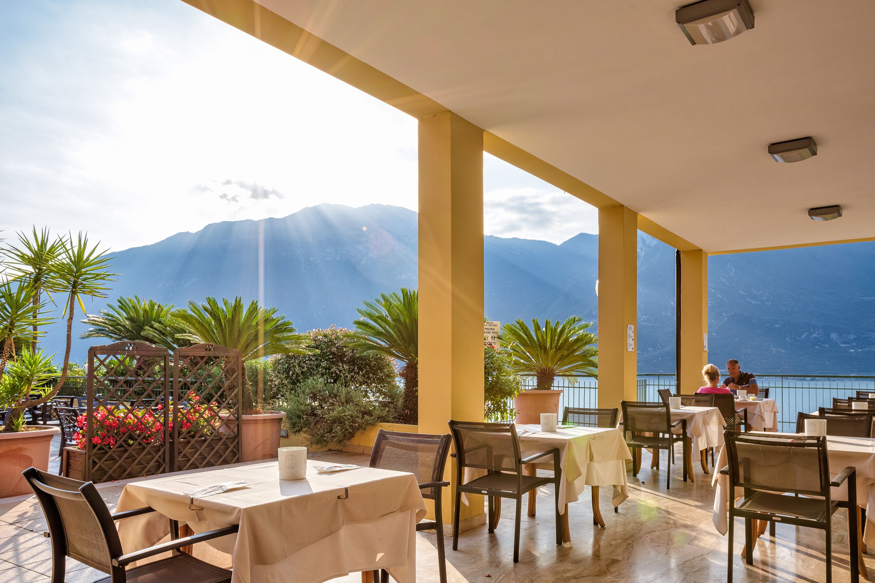 Un espace de restauration en plein air, avec des tables et des chaises, des plantes en pot et une vue sur les montagnes et la mer.