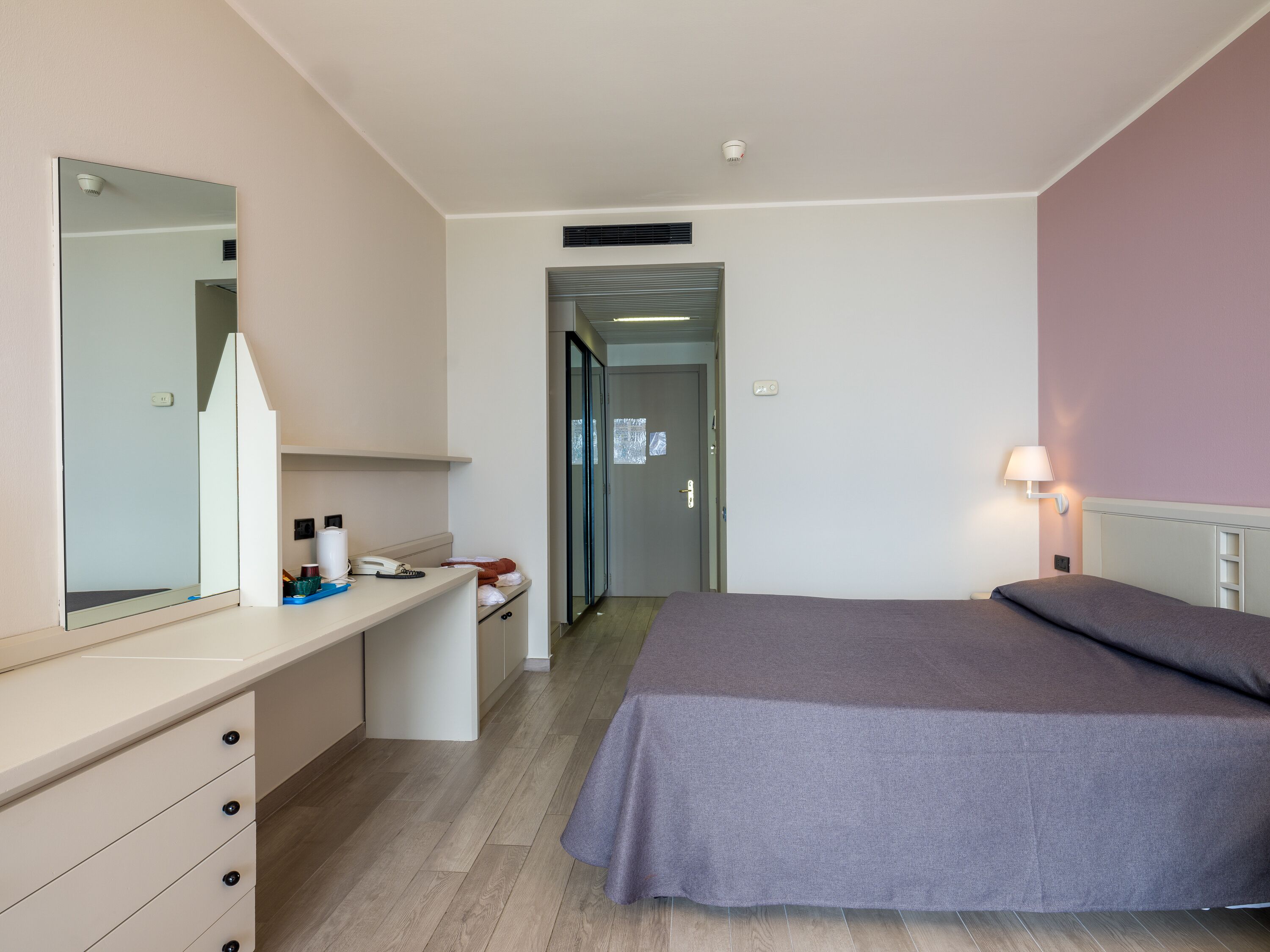 Ein Schlafzimmer mit Bett, Nachttisch, Spiegel, Lampe und Kleiderschrank.