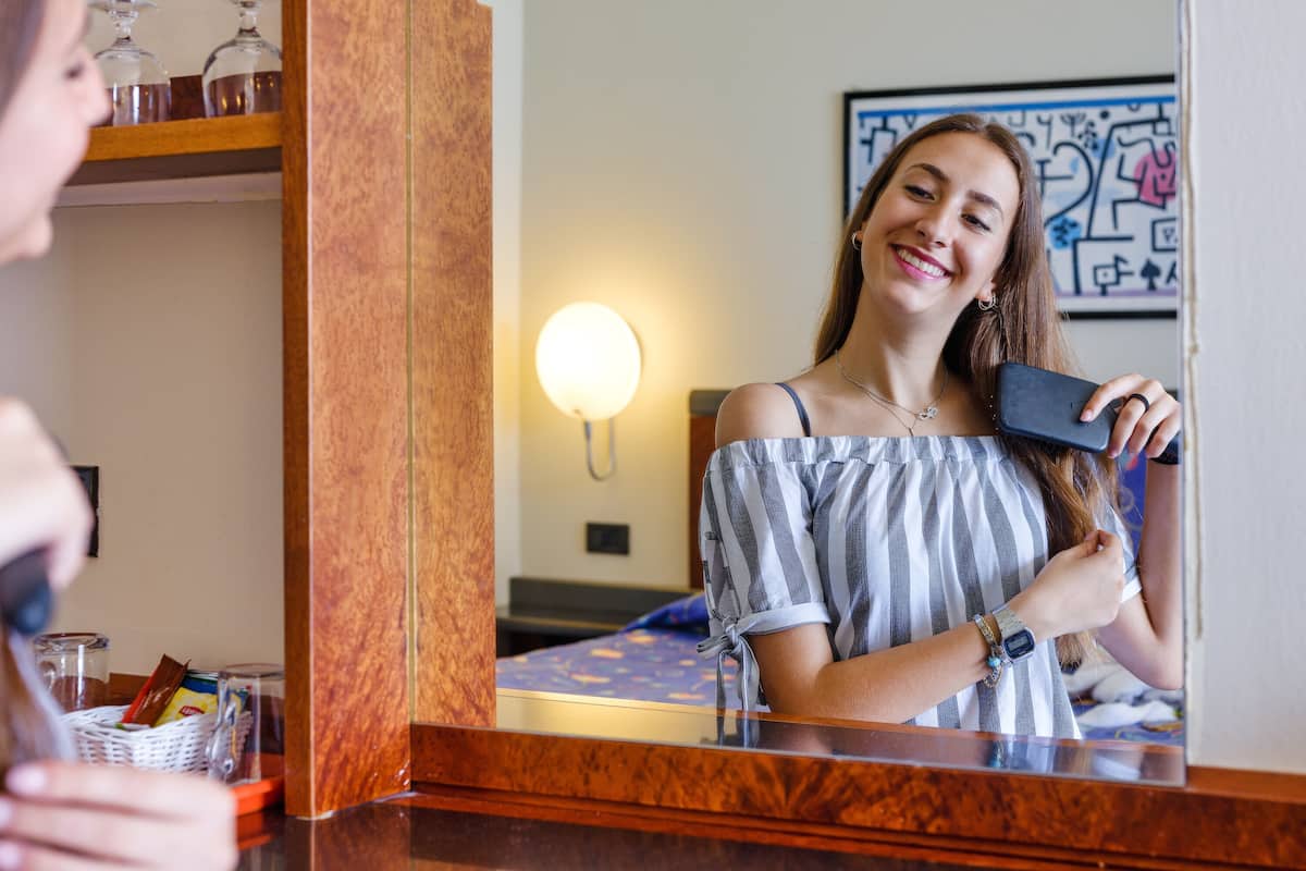 A hotel room with a wooden dresser, a mirror, and a bed with a blue bedspread.