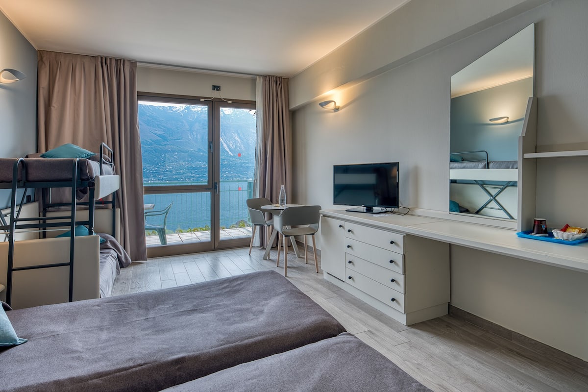 A modern hotel room with a balcony, a desk, a TV, and a bed.